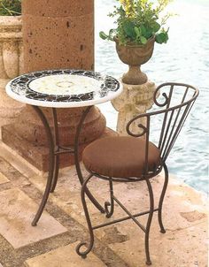 an outdoor table and chair with potted plant next to the water's edge