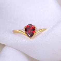 a close up of a ring with a red stone in it on a white cloth