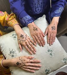 two women with henna tattoos on their hands are sitting on a cushion and touching each other's palms