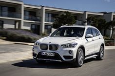 a white bmw suv is driving down the road in front of some apartment buildings with balconies