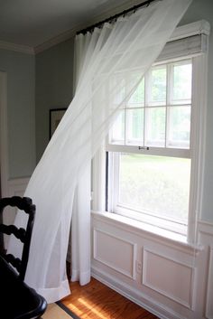 a chair sitting in front of a window next to a white drape on the wall