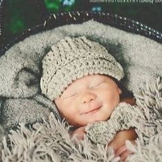 a baby wearing a knitted hat and sleeping in a basket filled with fluffy blankets