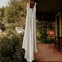 a white dress hanging from a clothes line on a porch with flowers and trees in the background