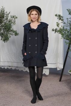 a woman standing in front of a white curtain wearing black tights and a hat