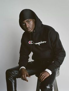 a man sitting on top of a stool wearing a champion hoodie and leather pants