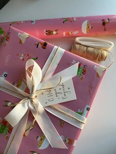 a pink wrapping paper wrapped in white ribbon next to a spool of twine