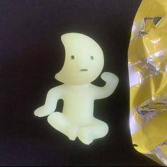 a plastic figure sitting next to a yellow wrapper on top of a black surface