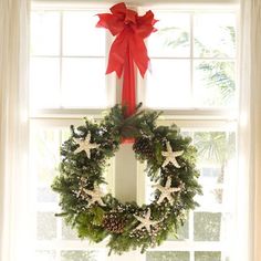 a christmas wreath hanging on the side of a window sill in front of a red bow