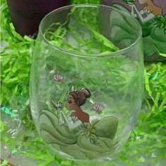 a glass with the image of princess and frog on it sitting in some green grass