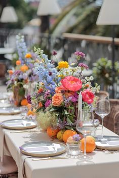 a vase filled with lots of colorful flowers on top of a table next to wine glasses