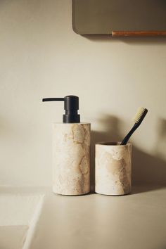 two marble containers with toothbrushes and soap dispenser sitting on a counter