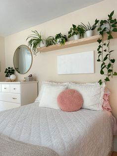 a white bed topped with lots of plants next to a wall mounted mirror and dresser