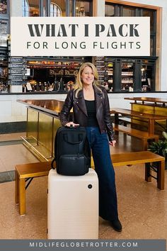 A woman stands with a beige roller bag and black backpack. She is wearing a brown moto jacket and jeans. Best Outfit For Long Flight, Travel Essentials Flight, Best Long Haul Flight Outfit, What To Take On A Long Flight, Carry On Essentials Long Flights, Long Flight Outfit Summer, Long Haul Flight Outfit Comfy, In Flight Essentials, Carry On Bag Essentials Long Flights