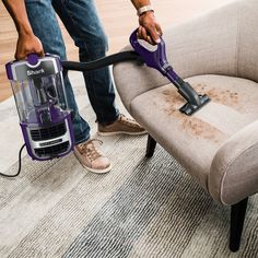 a person using a vacuum to clean a chair