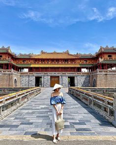 a woman wearing a hat standing in front of an old building with stone walkways