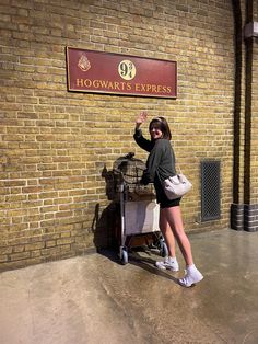 a woman standing in front of a hogwart's express sign with her hand up