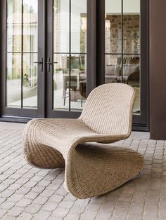 a wicker lounge chair sitting on top of a brick floor next to sliding glass doors