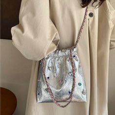 a woman wearing a white coat and holding a silver purse with beads on the handle