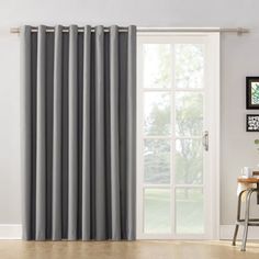 a living room with a large window covered in grey curtains and a wooden table next to it