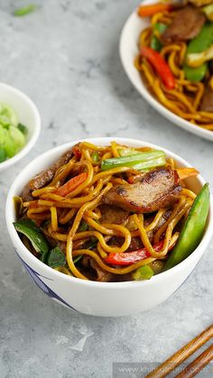 two white bowls filled with stir fry noodles and veggies next to chopsticks