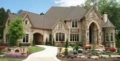 a large stone house with lots of windows and landscaping around the front door, along with flowers