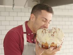 a man eating a doughnut with icing and nuts on it while wearing an apron