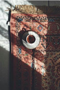 a cup of coffee sitting on top of a table next to a rug with an intricate design