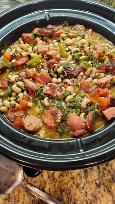 a crock pot filled with beans, ham and broccoli on top of a marble counter