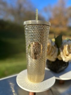 two gold cups sitting on top of a table next to each other with flowers in the background