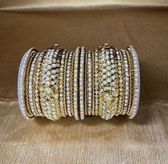 Model - MG1 Step into a world of sophisticated sparkle with this exquisite set of silver-finish bangles, each one a mini universe of dazzling rhinestones. Gleaming Mhendi Gold Charm: - The cool, timeless elegance of a Mehendi gold finish enhances any outfit, effortlessly transitioning from casual to dressy. - The metallic sheen catches the light beautifully, adding a touch of subtle shimmer to your wrist. Rhinestone Brilliance: - Each bangle dances with the light, thanks to an array of sparkling rhinestones meticulously set within the design. - The stones catch the light with every movement, creating a mesmerizing dance of brilliance. Note: Pictures are taken by phone and Color Shade may sometimes vary slightly from actual colors Brand Zenia Creations Product of India White Bangle With Diamond Accents For Gift, White Diamond Accented Bangle As A Gift, White Bangle With Diamond Accents As Gift, Silver Bangle With Rhinestones As Gift, Metal Bangle With Rhinestones As Gift, Metal Bangle With Rhinestones For Gift, Wedding Rhinestone Bangle, Silver Jeweled Cubic Zirconia Bangle, Luxury Gold Dazzling Bangle