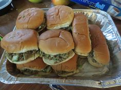 there are many sandwiches on tin foil in the middle of this table with apples behind them