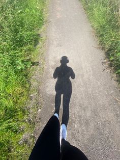 a person standing in the middle of a dirt road with their shadow on the ground