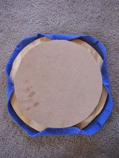 an empty wooden plate sitting on top of a blue cloth covered tablecloth in front of a carpeted floor