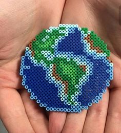 a hand holding a small beaded brooch in the shape of a planet on it's palm