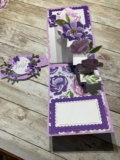 two cards with purple flowers on them sitting on a wooden table next to each other