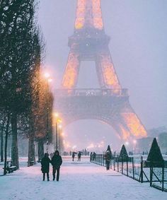 the eiffel tower is lit up in red and yellow on a snowy day