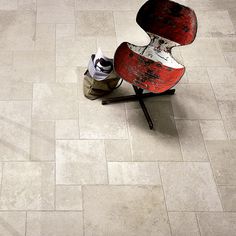 a red chair sitting on top of a white tiled floor next to a brown bag