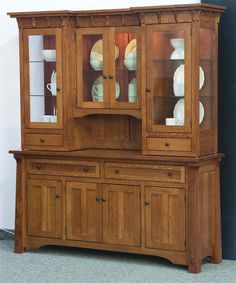 a wooden china cabinet with glass doors on the top and bottom, sitting against a wall