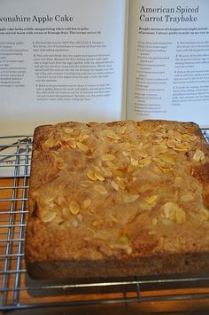 an open book sitting on top of a cooling rack next to a baked cake covered in nuts