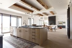 an open kitchen and dining room with wood beams on the ceiling, hardwood flooring, and white walls