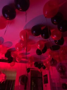 red and black balloons hanging from the ceiling in a room with pink lighting on it