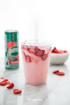 a drink in a plastic cup with strawberries on the side and a can of soda behind it