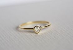 a gold ring with a heart shaped diamond in the center on a white surface,