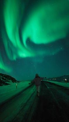 a person walking down a road under an aurora bore