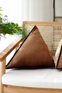 two pillows sitting on top of a wooden chair next to a potted plant