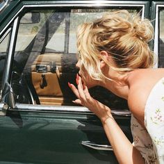 a woman leaning out the window of a green car with her hand on the door handle