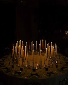 a table topped with lots of lit candles in the middle of a dark room filled with tables