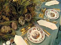 a table set for christmas dinner with place settings and pine cones on the table top