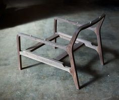 a small wooden bench sitting on top of a cement floor next to a black wall