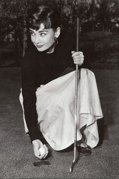 a black and white photo of a woman kneeling on the ground holding a golf club